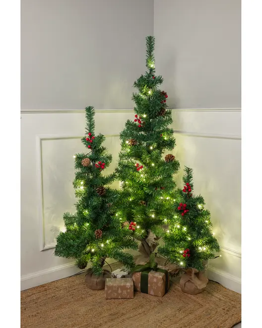 Set med tre konstgjorda julgranar med kottar, röda bär och varmvita LED-ljus. Granarna har jutesäck runt foten och små paket under.