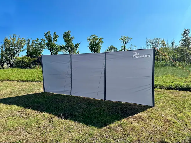 Udendørs vindskærm med tre sektioner, gråt stof, sort kant og Nakano-logo i hjørnet. Velegnet til camping eller have, giver læ og privatliv.