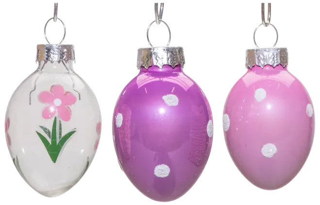Set med tre äggformade glaspynt med silvertoppar: en vit med rosa blomma, en lila med vita prickar och en rosa med vita prickar. Blank yta.