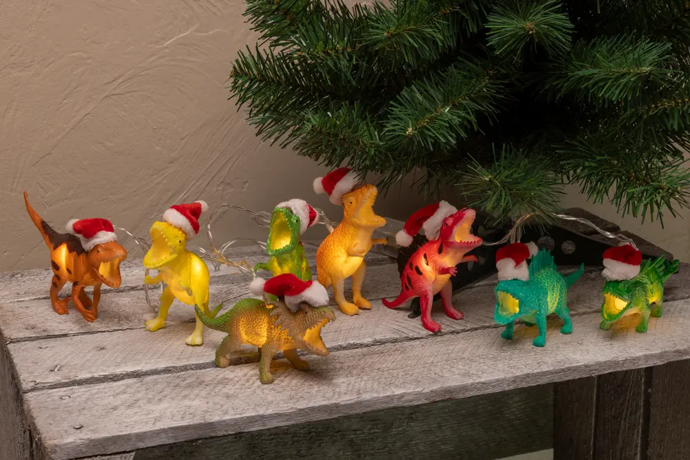 Ljusslinga med färgglada dinosauriefigurer, varje dinosaurie bär en liten röd tomteluva. Passar utmärkt som juldekoration inomhus eller runt granen.