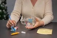Klar glasmugg med handmålade festliga motiv, inklusive blå stjärna och röda detaljer. Inkluderar små färgburkar, pensel, gul markeringspenna och designskiss på gult papper.