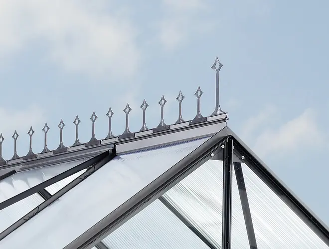 Dekorativ metallkam på växthusets tak med spetsiga spiror och klara polykarbonatpaneler, ger ett elegant viktorianskt utseende och skyddar mot väder.