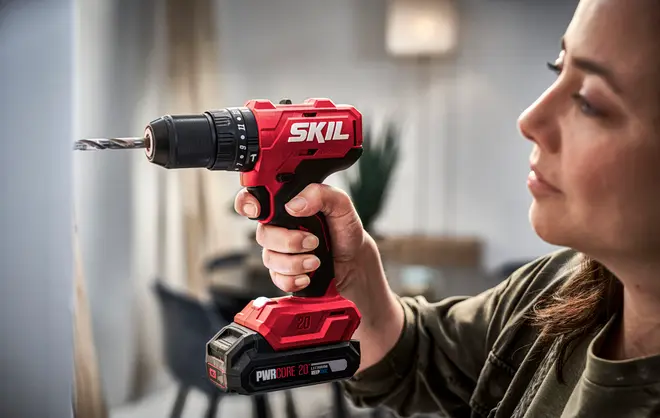 Rød SKIL batteridrevet boremaskine med sort greb, 20V batteri og metalbor. Ergonomisk design, egnet til hjemme- eller professionelt brug. Batteripakken er mærket PWRCORE 20.