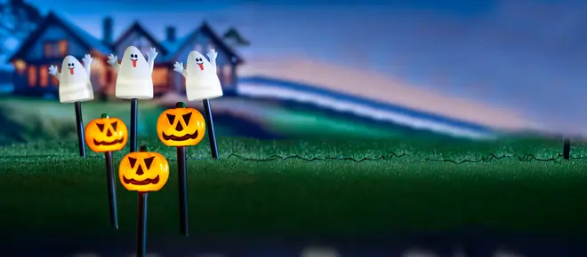 Halloween-trädgårdsdekorationer med tre spökfigurer och tre pumpalyktor på pinnar, perfekta för utomhusbruk, med ett hus i bakgrunden.