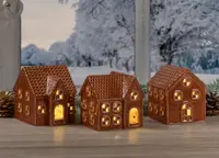Sæt med tre keramiske lysestager formet som honningkagehuse, detaljerede vinduer og døre, brun finish, udsender varm glød, perfekt til juledekoration på borde eller hylder.