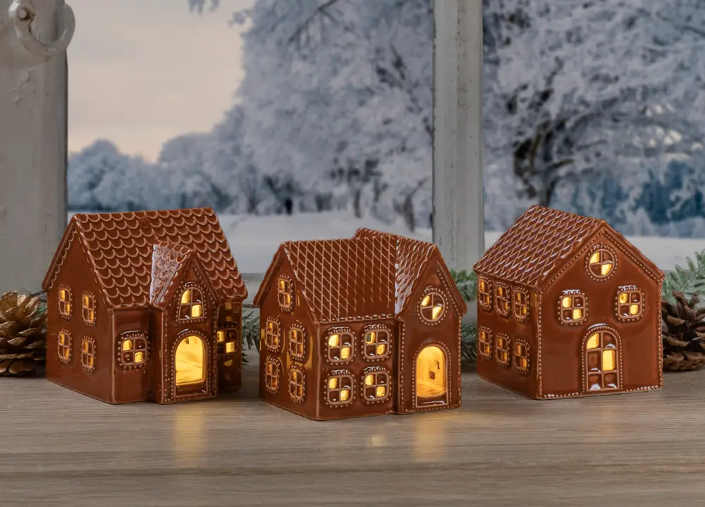 Sæt med tre keramiske lysestager formet som honningkagehuse, detaljerede vinduer og døre, brun finish, udsender varm glød, perfekt til juledekoration på borde eller hylder.