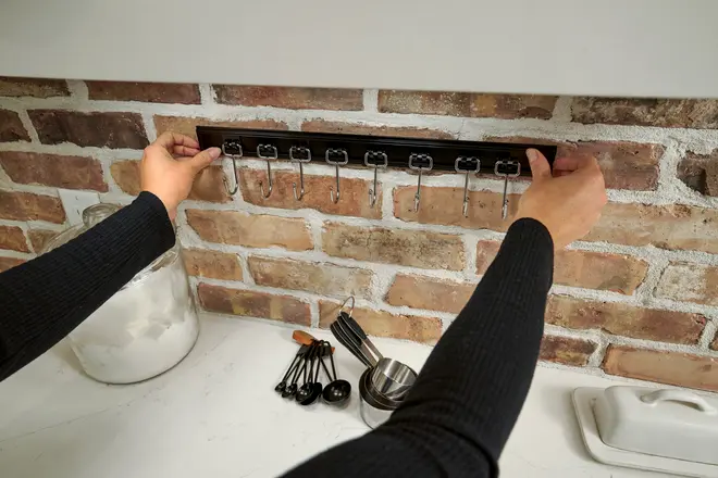 Vægmonteret sort metalstativ med otte kroge, perfekt til ophængning af køkkenredskaber. Elegant design, nem montering, ideel til måleskeer, kopper eller små køkkenredskaber.