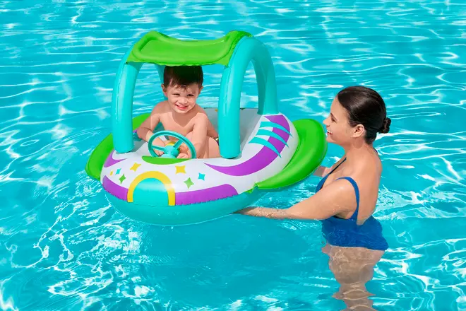 Oppustelig badebåd formet som bil med tag, rat og farverigt design. Velegnet til små børn, giver skygge og støtte under leg i vandet.