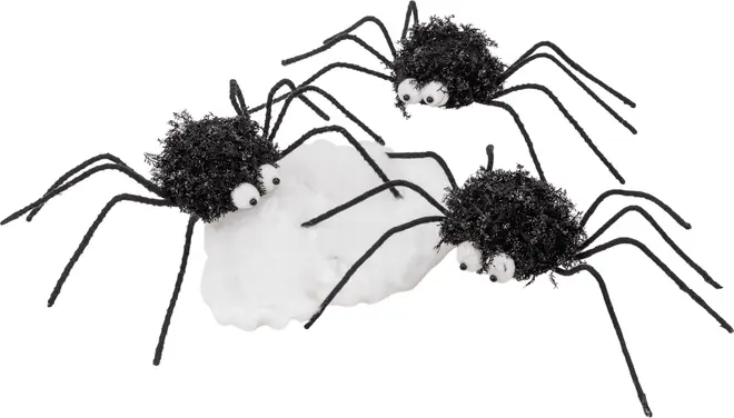 Set med tre fluffiga svarta spindeldekorationer med rullande ögon och böjbara ben, placerade runt en vit spindelnätsbas. Perfekt för Halloween eller temafest.