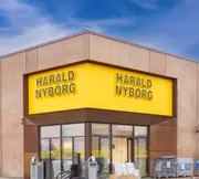 Stor Harald Nyborg butik med gul skiltning, glasindgang og udendørs udstilling af forskellige byggematerialer og produkter på paller og stativer.