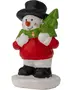 Festlig snemand figur med rød sweater, sort hat og støvler, holder et grønt juletræ. Har smilende ansigt med orange næse og røde kinder, står på hvid base.