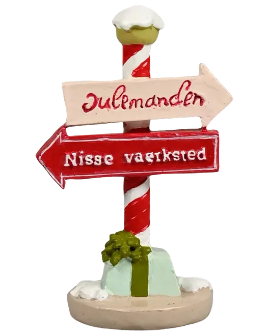Juledekorationsfigur med rød-hvid stribet stolpe, to retningsskilte, sne detaljer og en grøn gave ved basen. Skiltene viser 'Julemanden' og 'Nisse værksted'.