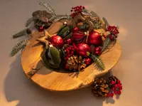 Träskål fylld med juldekorationer, kottar, konstgjorda bär och grankvistar. Dekorationerna inkluderar röda och gröna kulor, en guldfärgad stjärna och ett trä-hjärta.