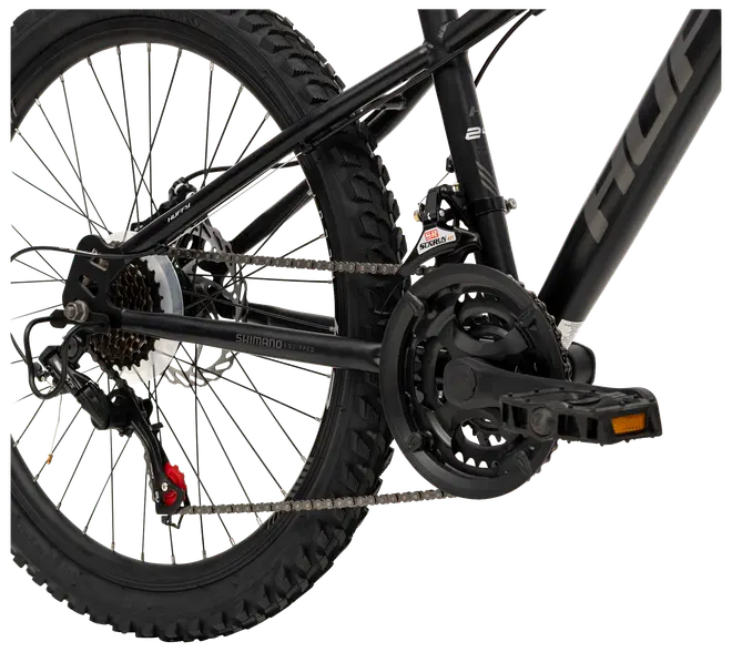 Närbild på svart mountainbike-drivlina med Shimano-växlar, kedja, pedaler och grovt bakdäck. Flera kugghjul och robust ram för terrängcykling.