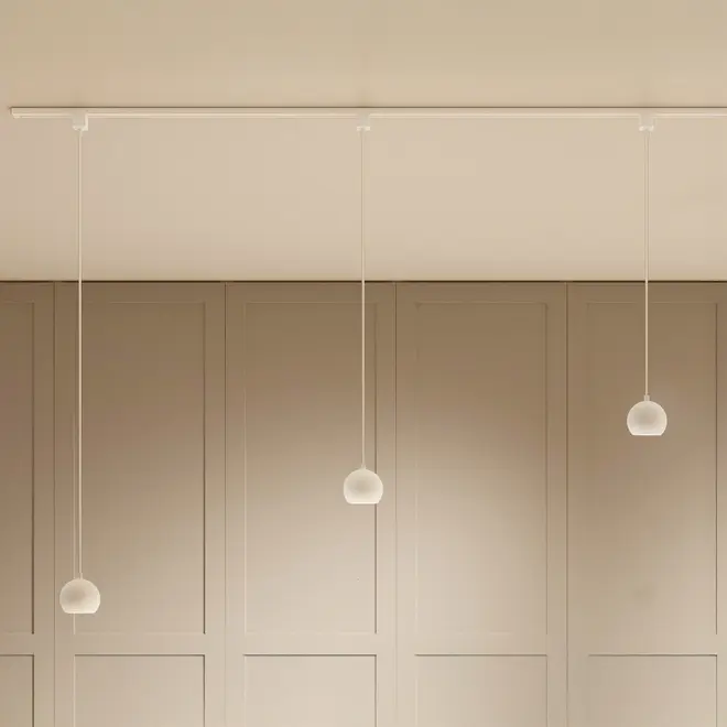 Minimalistisk pendellampe med tre matte glaskupler, ophængt fra en slank hvid skinne i loftet. Moderne design, ideel til køkken eller spisestue, giver blødt lys.