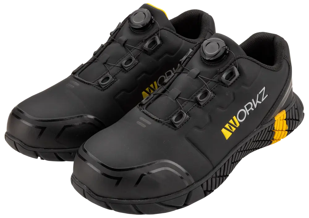Svarta arbetsskor med förstärkt tå, halksäker sula, gula detaljer och snabbsnörning med vred. Hållbar design för industriell användning. 'WORKZ' tryckt på sidan.