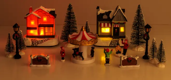 Miniatyr-julby med två upplysta hus, karusell, figurer, lyktstolpar och snötäckta träd. Detaljerad, festlig dekoration för jul- eller modellscener.