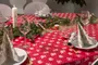 Rødt juledug med hvide og gyldne festlige mønstre, dækket på spisebord med tallerkener, guldbestik, foldede servietter, vinglas og gran-guirlande som midterpynt.
