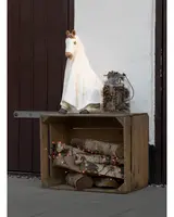 Trälåda med björkved dekorerad med orange ljusslinga. Ovanpå står en hästfigur täckt med vitt tyg och en glasburk fylld med kottar och kvistar.