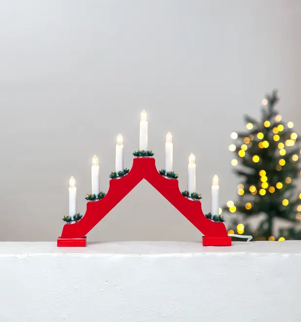 Rød elektrisk lysestage i træ med syv hvide LED-lys, hver pyntet med grønne kranse ved bunden. Perfekt til juledekoration i vindue eller på bord. Tilsluttes strøm.