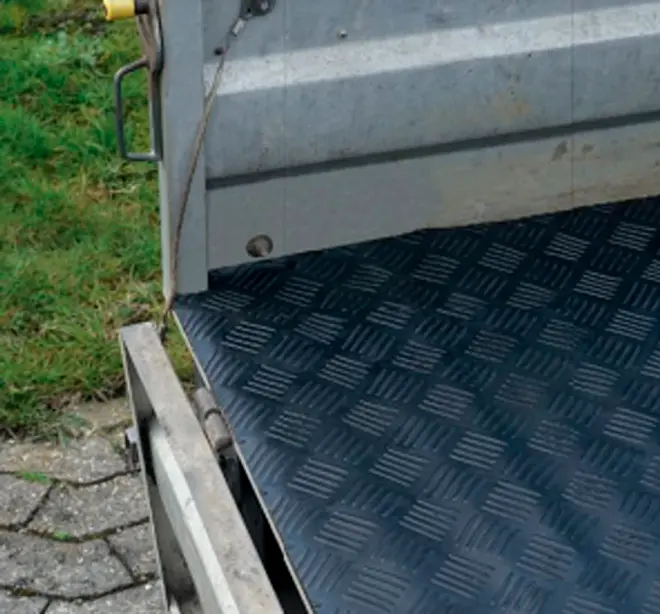 Närbild av en grå metallsläp eller lastbilsflak med svart durkplåtgolv och sidolås.