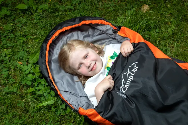 Børnesovepose med sort og orange ydre, gråt for og "CampOut"-logo. Velegnet til udendørs brug, giver varme og komfort til camping eller overnatning.