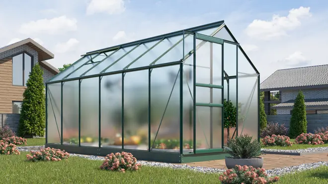 Rektangulärt växthus med grön metallram och genomskinliga paneler, sadeltak, dörr på ena sidan. Omgivet av trädgård med blommor och buskar, perfekt för året-runt odling.