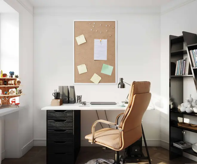 Moderne hjemmekontor med ergonomisk stol i beige, hvidt skrivebord med sorte skuffer, opslagstavle, skrivebordslampe og organiseret kontorartikler. Reol og vinduesplads i baggrunden.