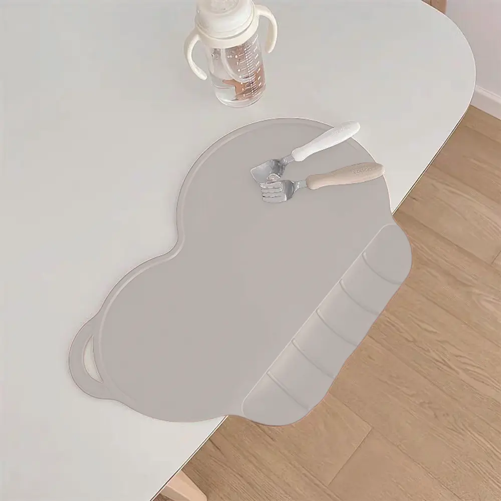 Grå silikone dækkeserviet formet som en sky med forhøjet kant, designet til børn. Inkluderer gaffel og ske med hvide håndtag samt en sutteflaske. Passer på bordhjørne.