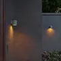 Moderne cylindriske udendørs væglamper i mat grå finish, monteret på betonvæg, udsender varmt nedadgående lys. Velegnet til have eller terrasse, vejrbestandigt design.