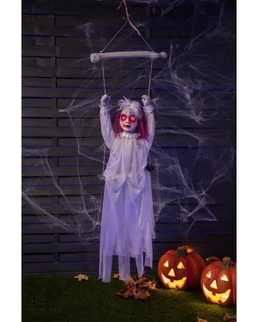 Hängande spökdekoration med lysande röda ögon, vit trasig klänning och skrämmande ansikte. Inkluderar gunga, perfekt för Halloween. Två snidade pumpor bredvid.