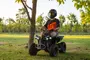 Sort mini-ATV til børn med fire grove dæk, forlygter og styr. Egnet til udendørs brug. Vist med barn iført hjelm og briller.