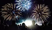 En menneskemængde ser et farverigt fyrværkerishow om natten med store blå og gyldne eksplosioner, der oplyser den mørke himmel.