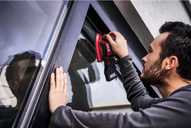 Röd och svart SKIL sladdlös fönstervakuum används på glasfönster. Ergonomiskt handtag, kompakt design, perfekt för effektiv rengöring av fönster och släta ytor.