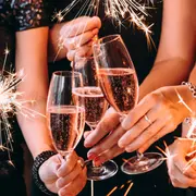 Tre händer håller champagneglas med mousserande rosé, omgivna av gnistrande tomtebloss. Skapar en festlig och firande stämning, perfekt för speciella tillfällen.