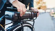 Nærbillede af en person, der monterer et aftageligt batteri på bagagebæreren af en elcykel, hvilket viser batteriets sikre pasform og brugervenlige design.