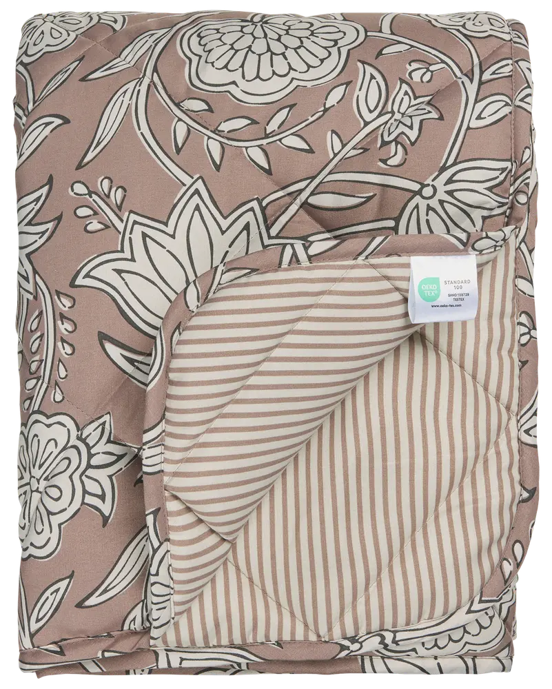 Vatteret tæppe med brun og hvidt blomsterprint på den ene side, beige og hvide striber på bagsiden, blød tekstur og synligt plejemærke. Velegnet til seng eller dekoration.