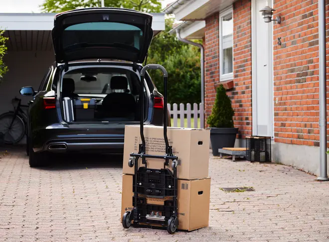 Sammenklappelig sort sækkevogn med to hjul, vist oprejst og læsset med to papkasser. Perfekt til flytning eller transport af tunge genstande. Kompakt og bærbar.