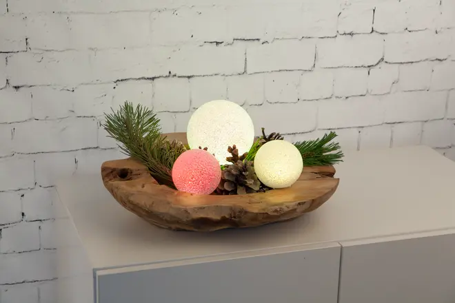 Dekorativt midtpunkt med tre lysende LED-kugler i hvid og pink, kunstige grangrene og kogler, arrangeret i en rustik træskål. Perfekt til festlig eller vinterlig dekoration.