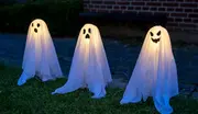 Set med tre utomhus Halloween-spökdekorationer med inbyggda lampor, vitt tyg över stommar och svarta ansikten, perfekta för trädgård eller gräsmatta.