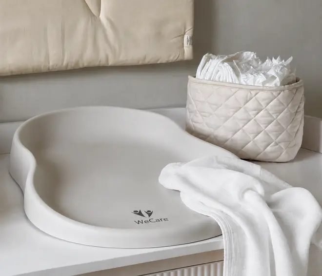 Cremefarvet polstret baby puslepude med hævede kanter, vist ved siden af en quiltet opbevaringskurv og et sammenfoldet hvidt håndklæde. - Billedet er skabt med AI