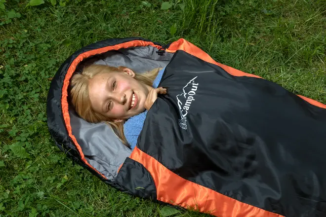 Sort og orange CampOut sovepose med hætte, velegnet til udendørs camping. Vist på græs, har lynlåslukning og isoleret foring for varme og komfort.
