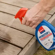 Billede af sprayflaske med rød dyse til fjernelse af myrer, sprøjtes på udendørs træterrasse.