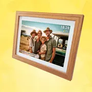 Digital fotoramme i træ med familiefoto, tids- og vejrvisning på hvid ramme, vist i skrå vinkel.