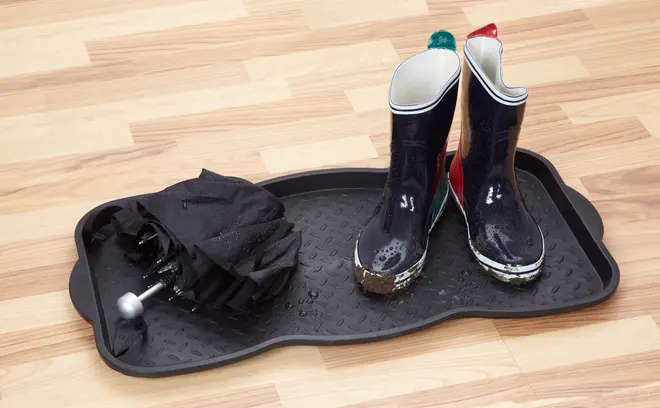 Svart vattentät bricka med upphöjda kanter, innehåller ett par blöta gummistövlar och ett hopfällt blött paraply. Skyddar golvet från vatten, lera och smuts.