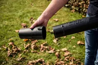 Närbild av en person som monterar ett svart SKIL lövblåsarrör med klickfäste, utformat för enkel hantering och effektiv trädgårdsrengöring.