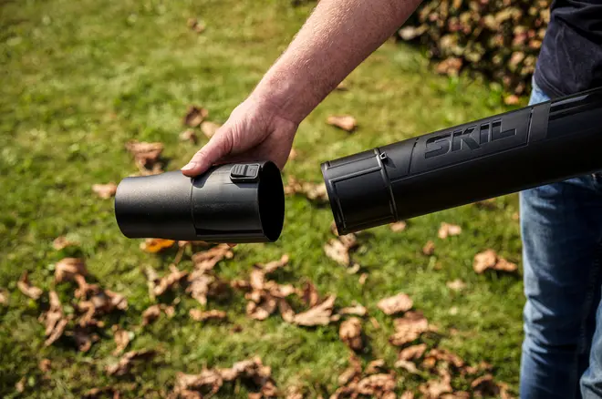 Nærbillede af en person, der samler et sort SKIL løvblæserrør med kliklås, designet til nem montering og effektiv rengøring af havearealer.