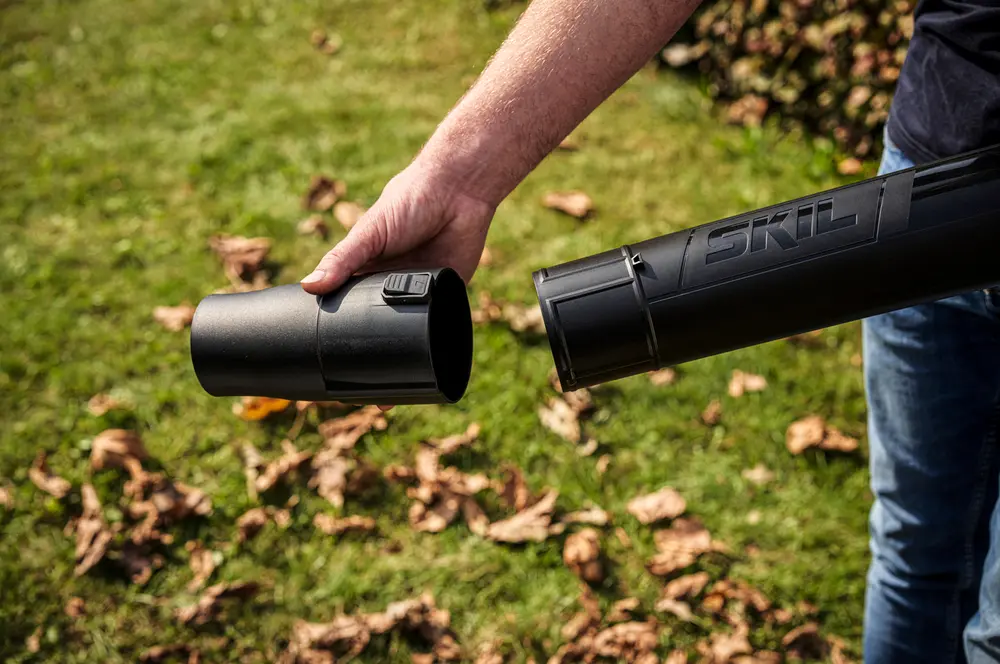 Närbild av en person som monterar ett svart SKIL lövblåsarrör med klickfäste, utformat för enkel hantering och effektiv trädgårdsrengöring.