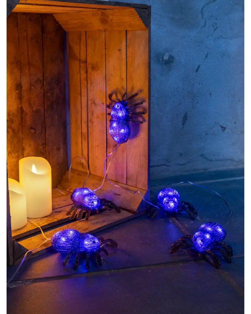 Ljusslinga med lila LED-spindlar och svarta ben, perfekt för Halloween eller temafester. Batteridriven, passar för inomhusdekoration. Flera spindlar på genomskinlig sladd.