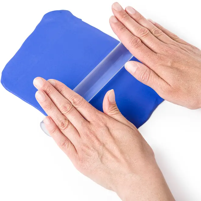 Klar akryl kagerulle bruges til at rulle blå fondant eller dej ud. Glat, cylindrisk design, ideel til kagedekoration eller bagning. Hænder viser brugen.